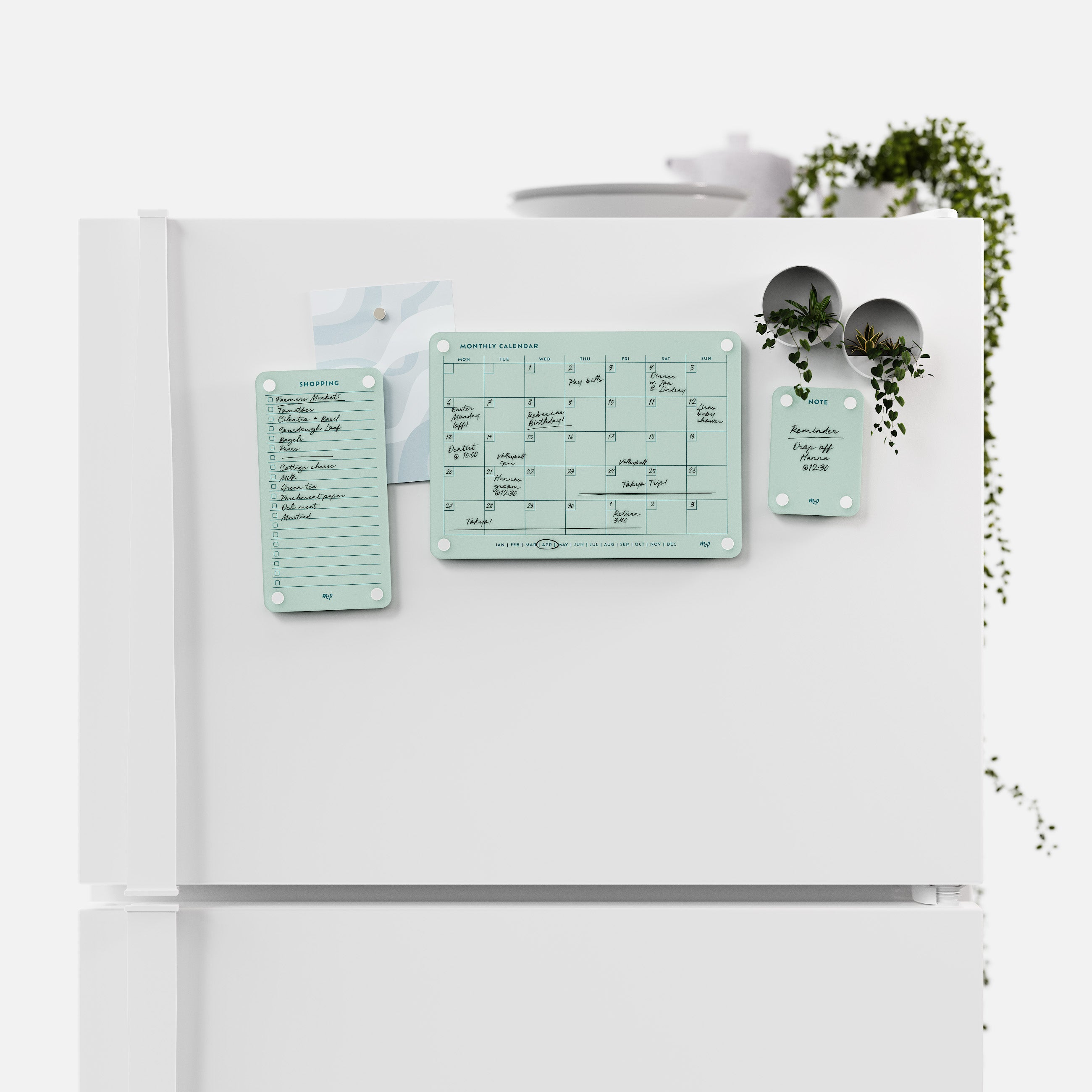 Seafoam green shopping list, monthly calendar and note board arranged across a white fridge door